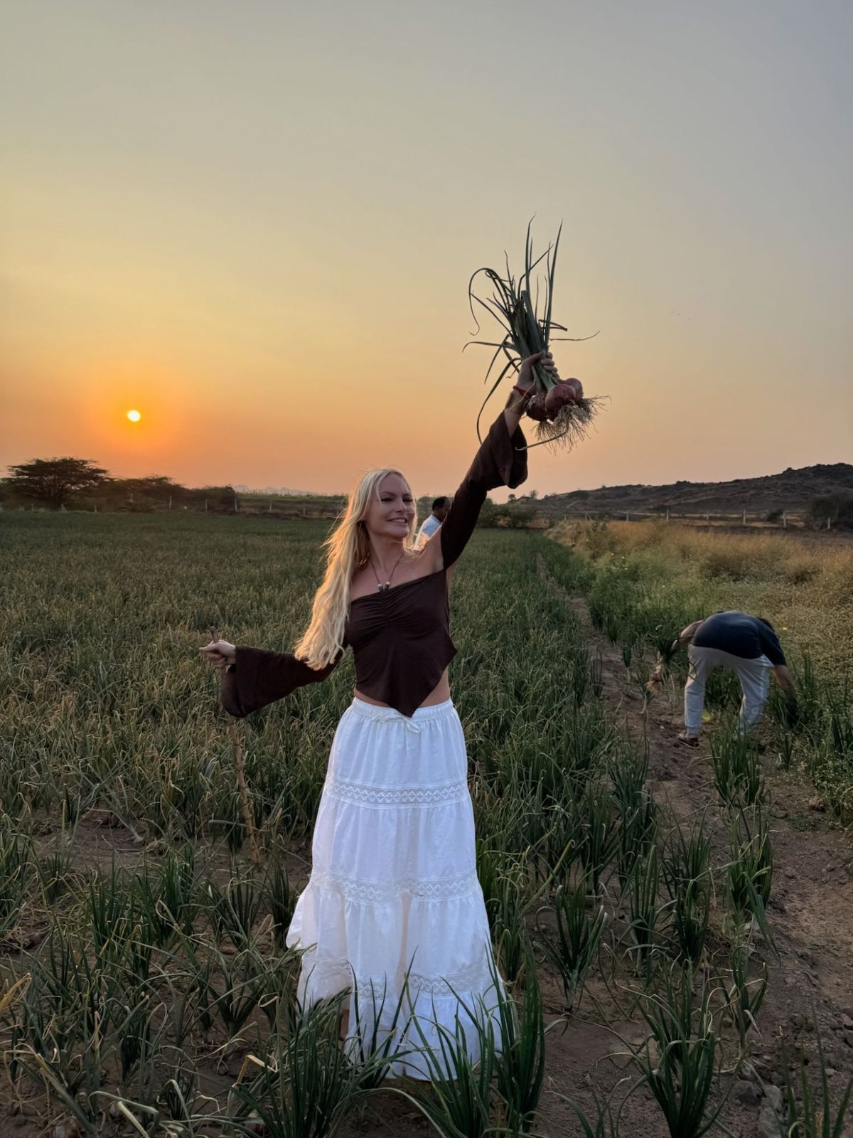 A guest holding up freshly pulled onions in the field at sunset