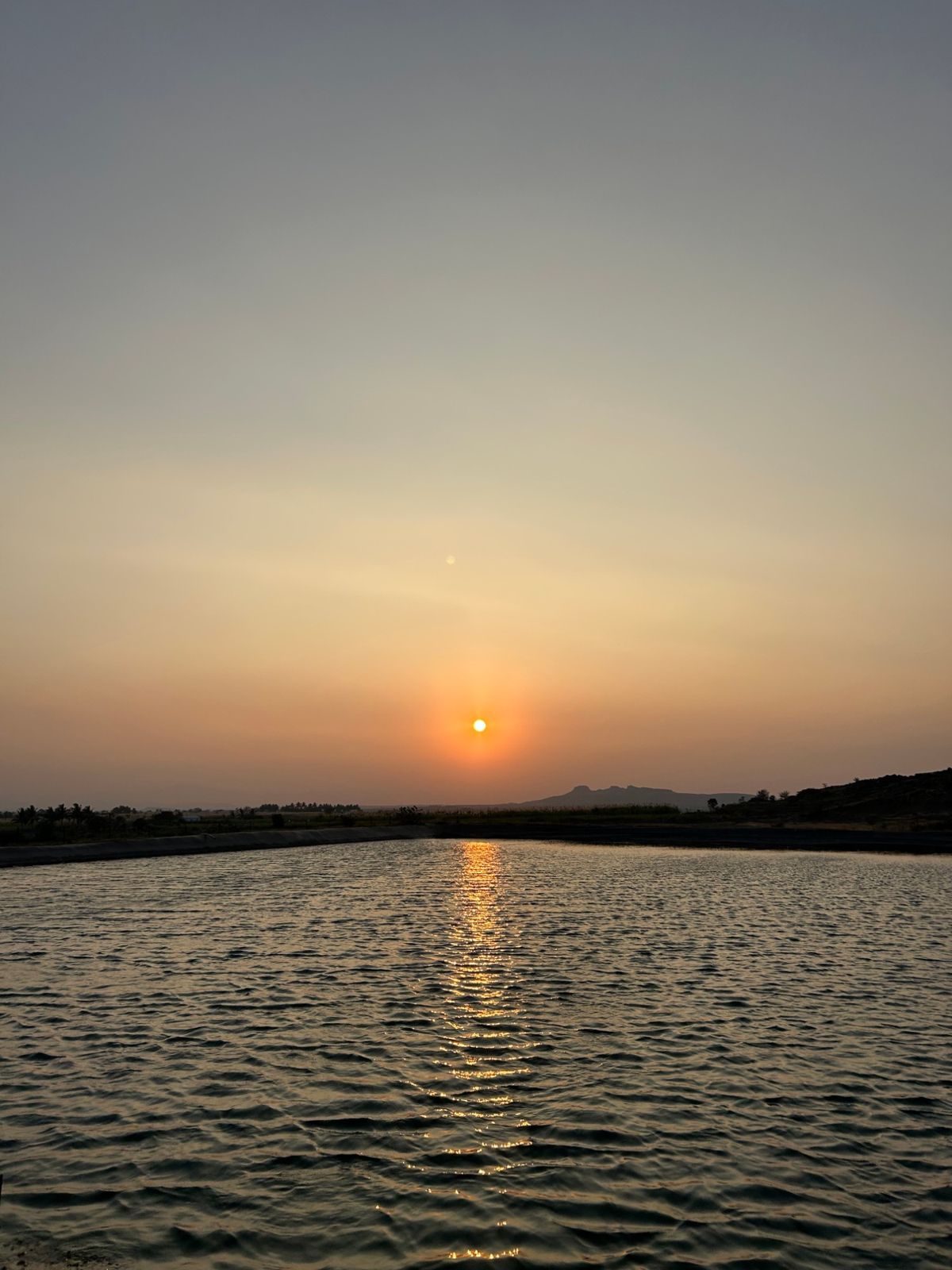 The sun setting over the farm pond with hills on the horizon